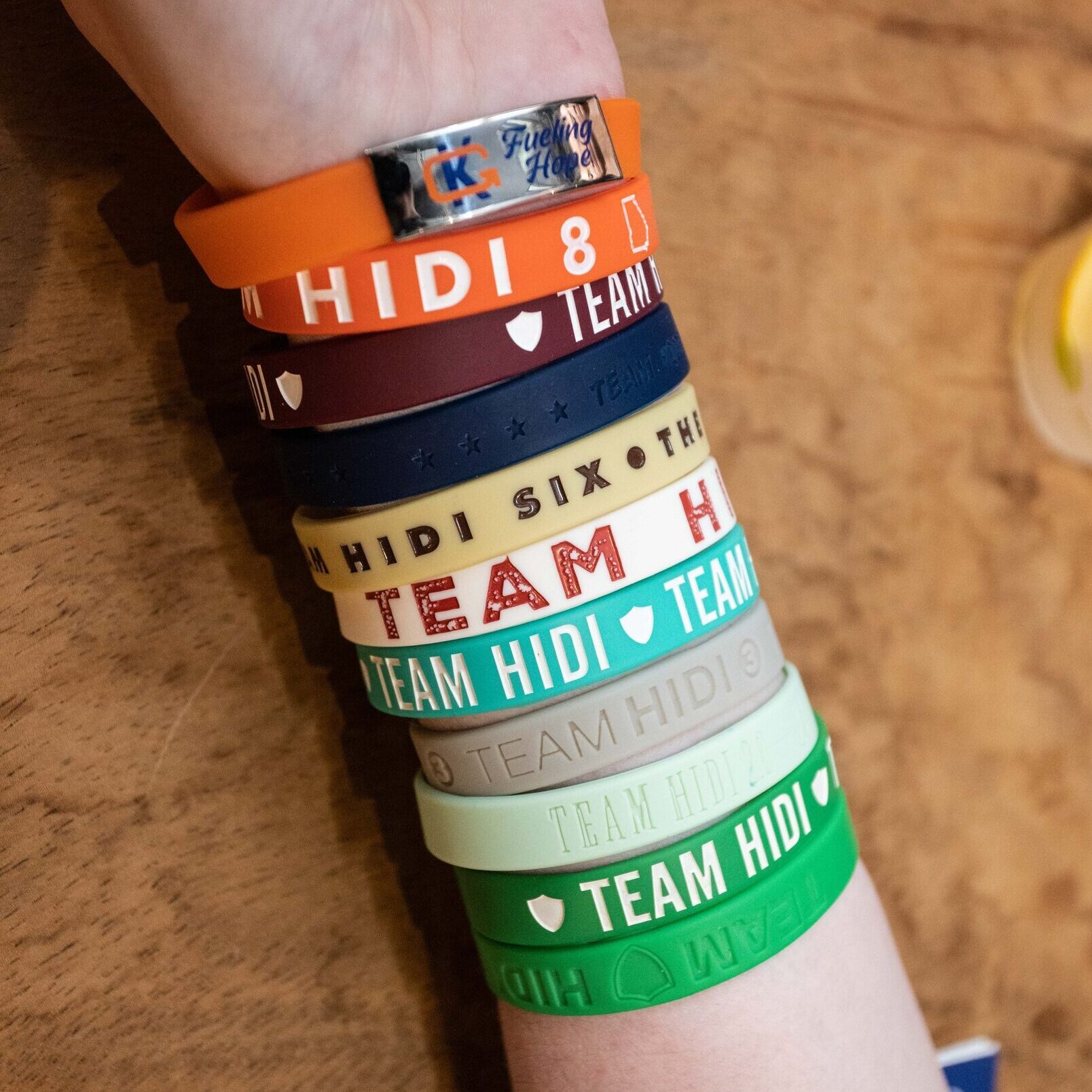 A person wearing wristbands from the first ten Team Hidi events on one arm