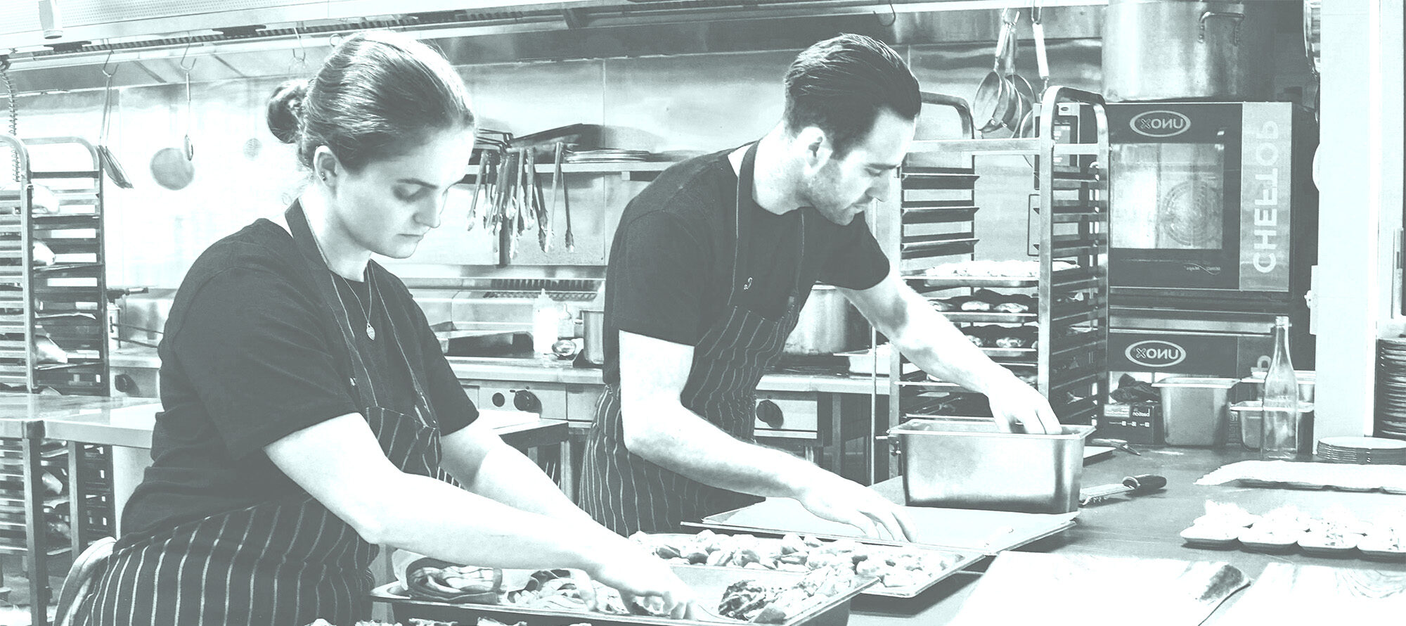Two chefs prep oysters in a kitchen