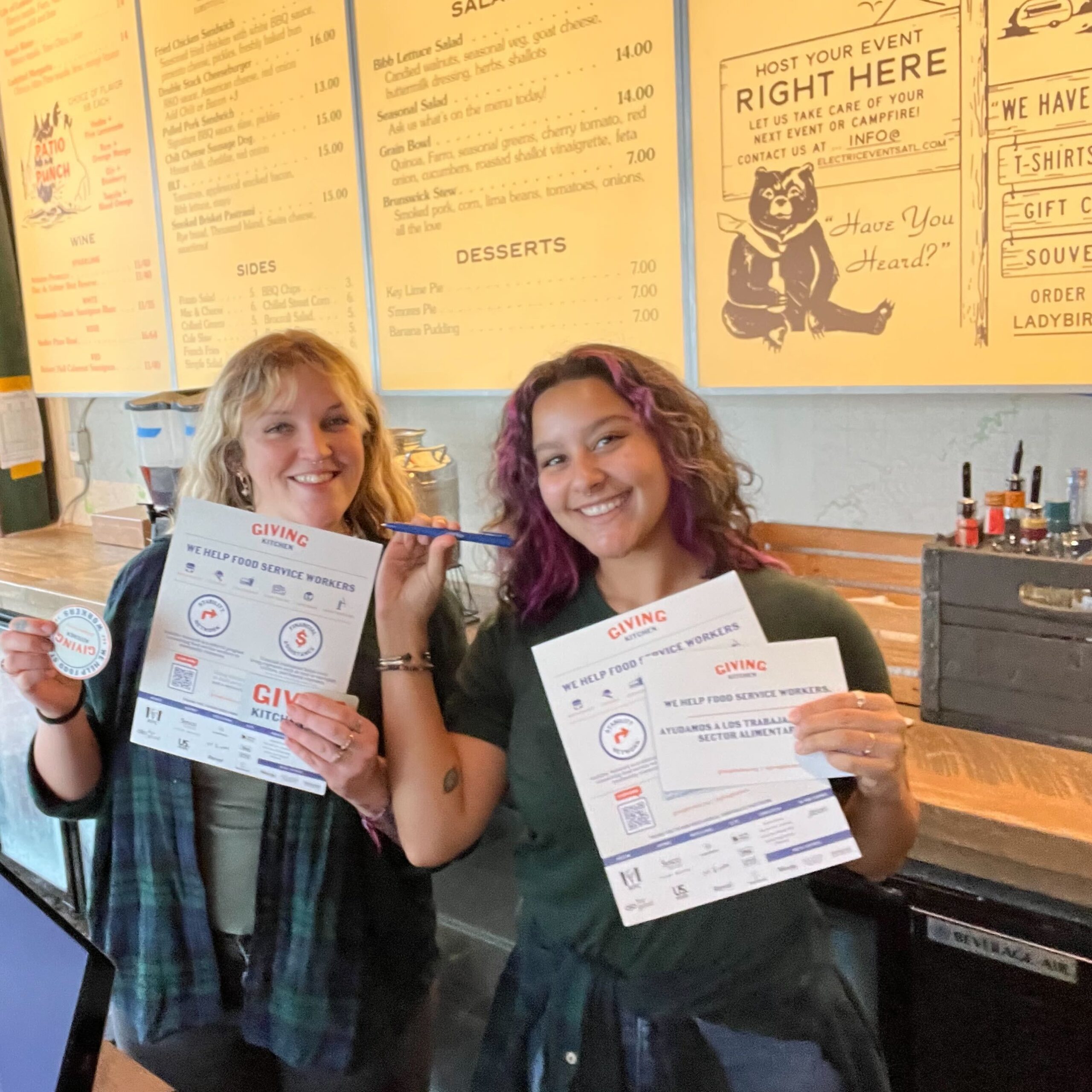 Cashiers at a coffee shop hold up Giving Kitchen swag
